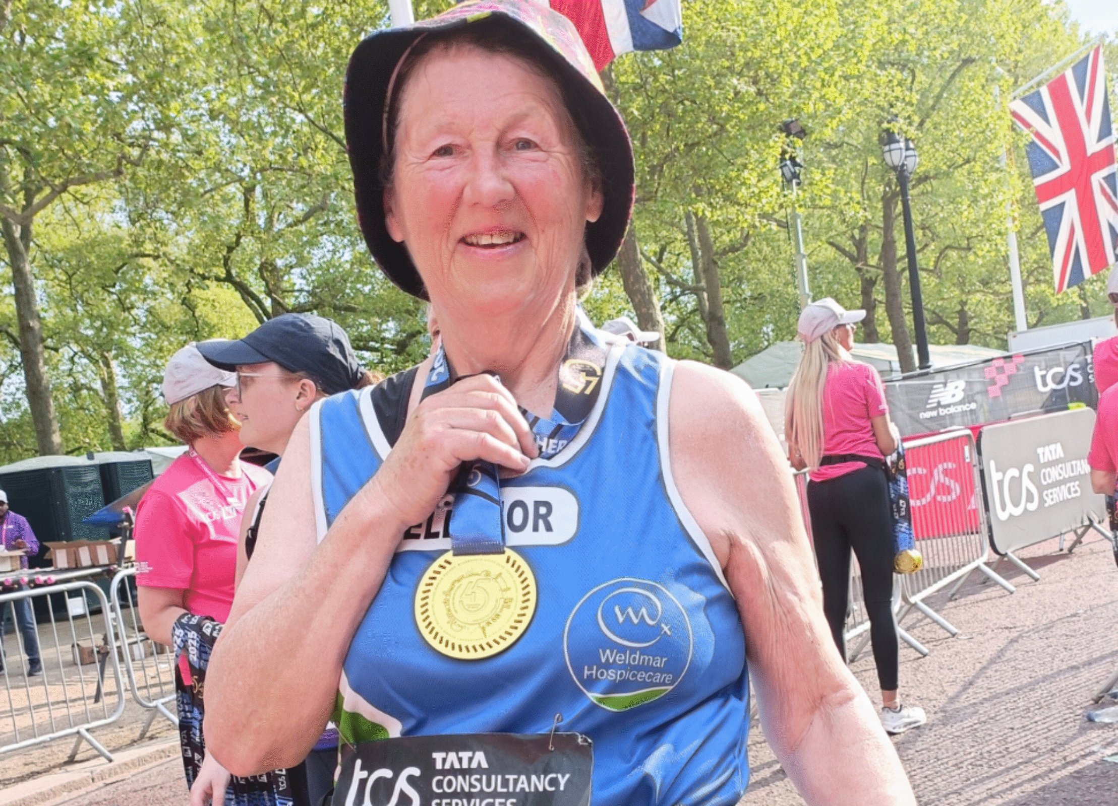 A picture of a smiling Eleanor wearing a Weldmar vest and holding her medal after completing the TCS London Marathon 2025