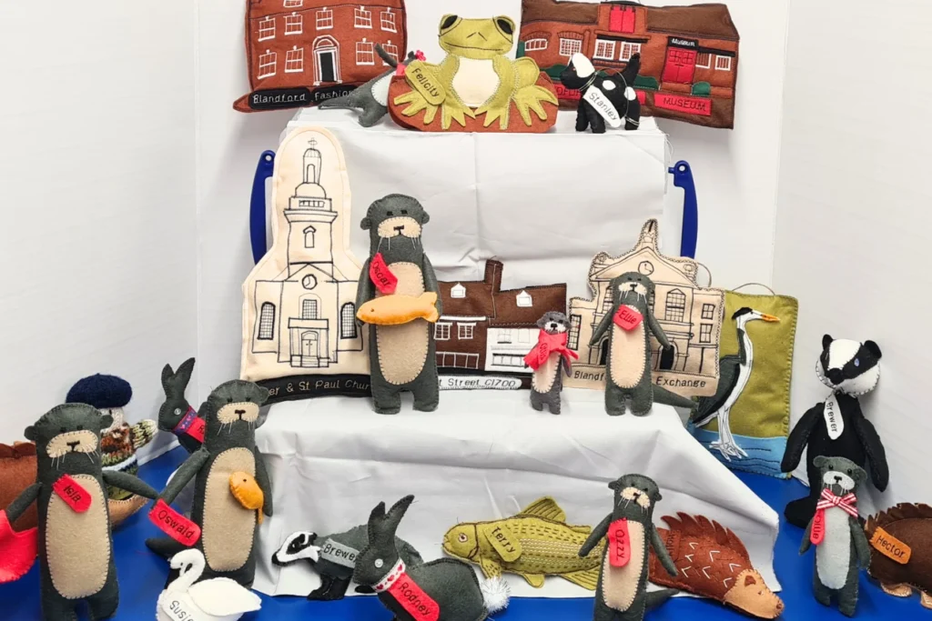 A selection of hand-sewn characters and buildings from Blandford Forum including otters, frogs, fish, hedgehogs, badgers, Blandford Museum and Blandford Fashion Museum