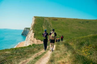 People walking along the Jurassic Coast taking part in the Jurassic Coast Ultra Challenge, cliffs in the distance and a bright blue sky.