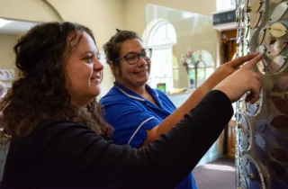 A nurse and a woman point to a leaf on Weldmar's Memory Tree